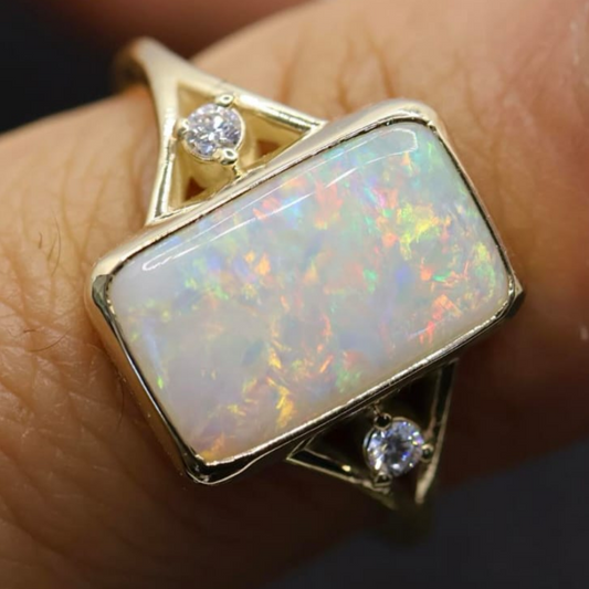 Gold ring with a large opal stone and smaller diamonds on a finger