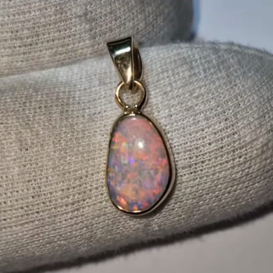 Opal pendant in a gold setting on a textured gray surface